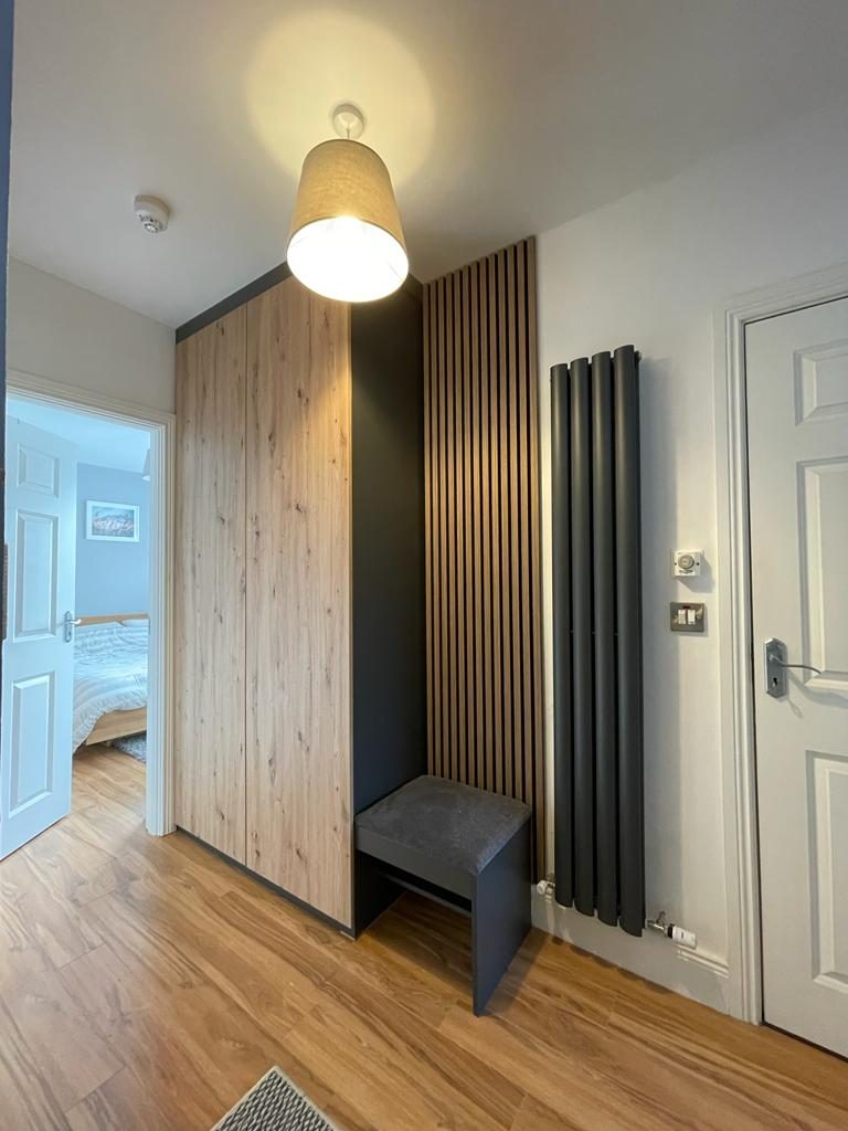 A hallway with a timber-clad unit, a slatted panel, a bench and a column radiator