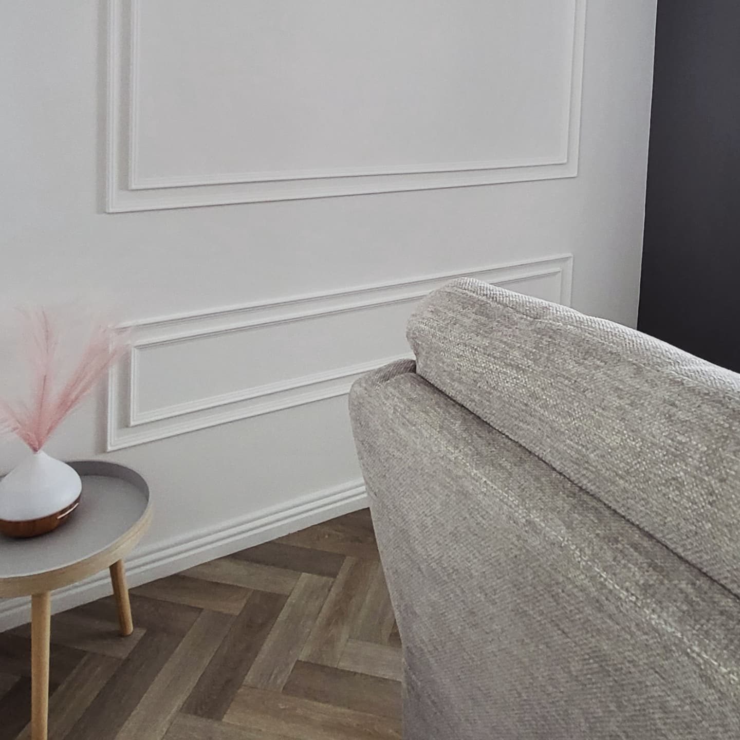 White box moulding panels on a wall above a herringbone floor, a grey armchair in the corner