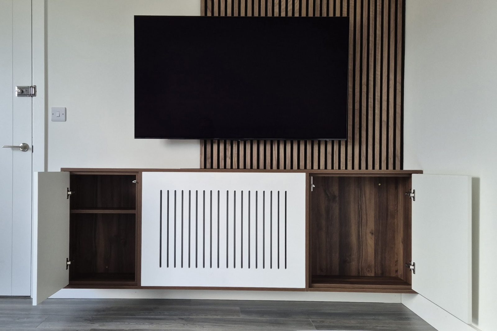 A media wall with a slatted timber panel, a wall-mounted TV and a floating unit with walnut doors