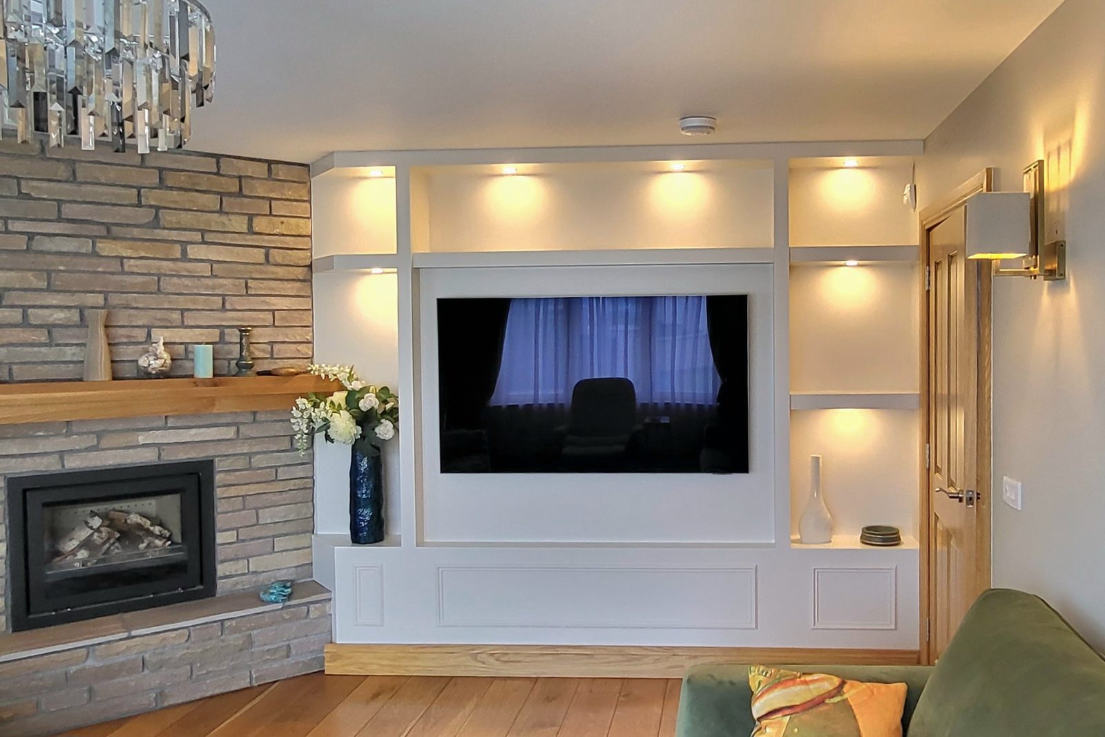 Living room built-ins with lit shelves around a TV beside a stone-clad fireplace wall