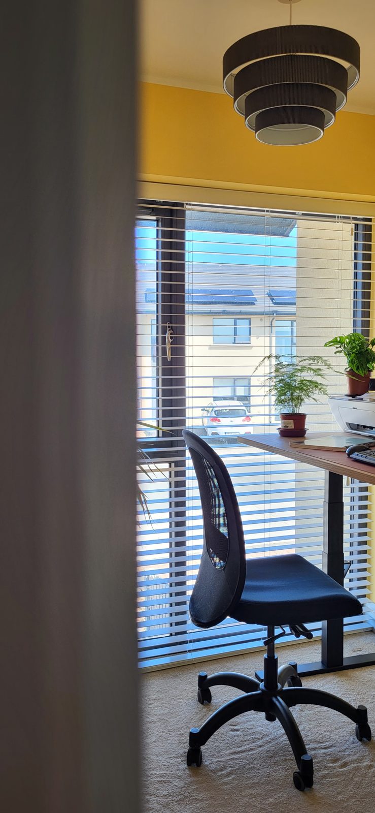 A home office corner with a desk and chair by a tall window