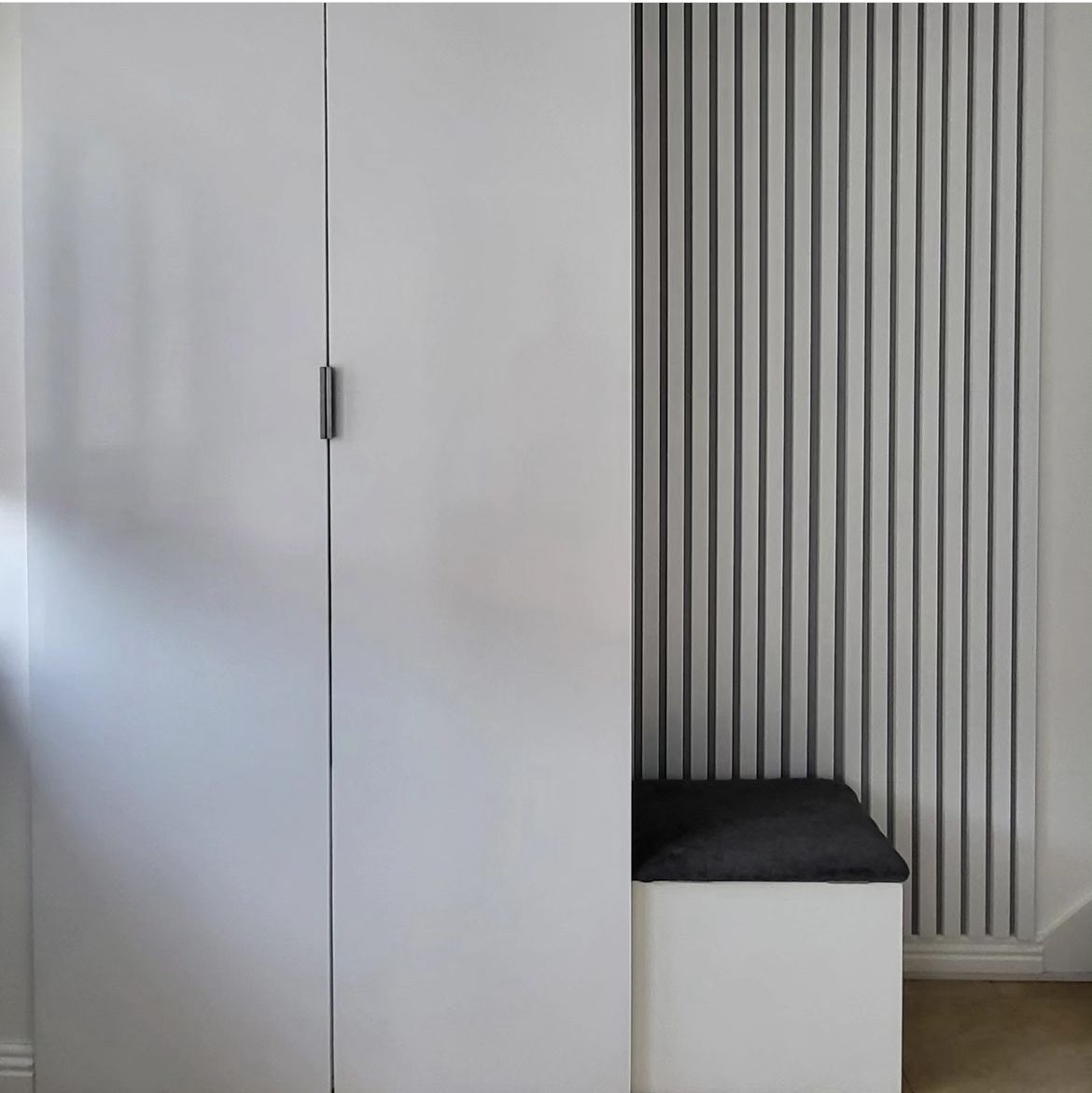 Tall white wardrobe doors beside a slatted panel and a bench seat