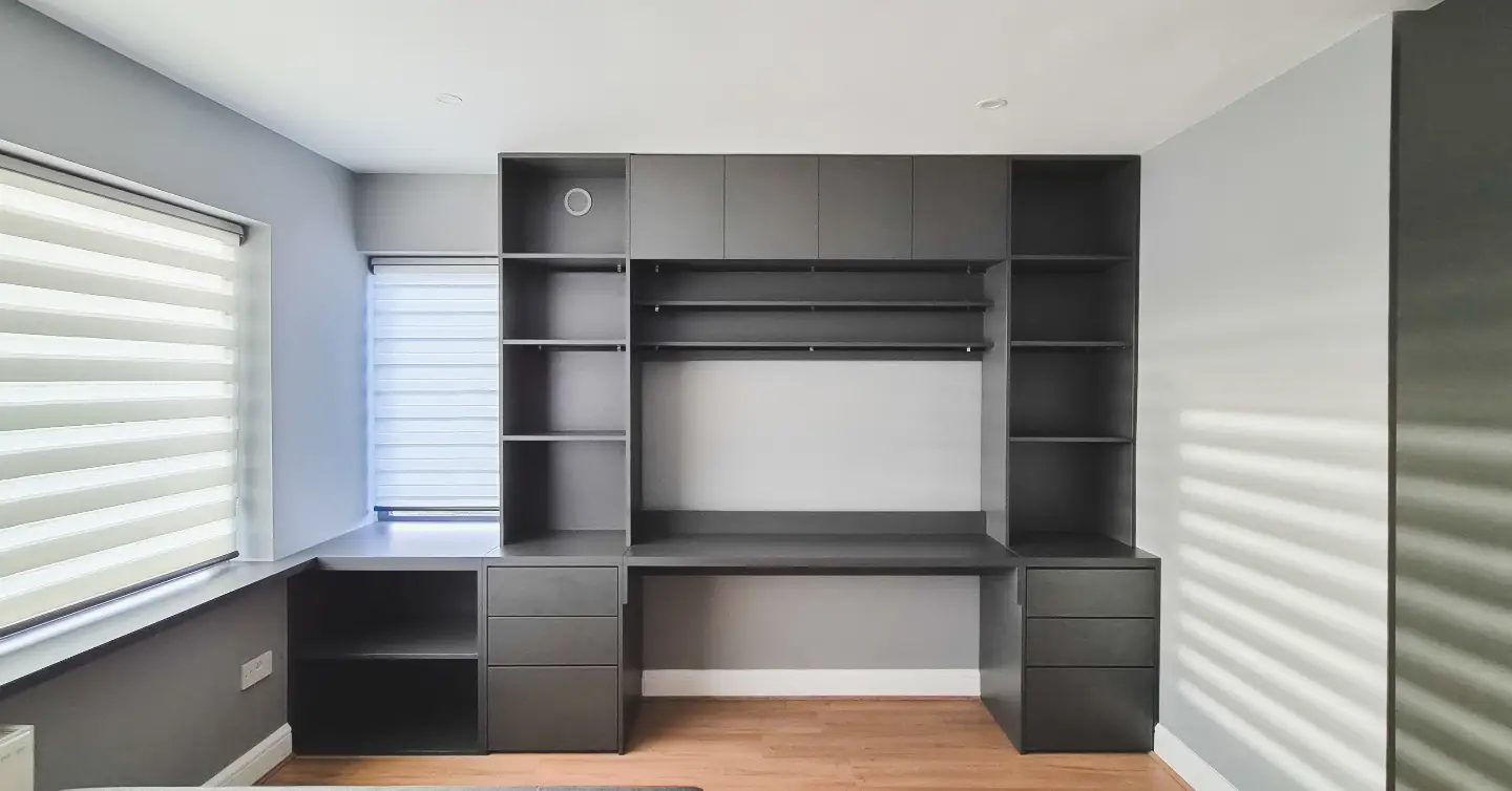 A dark grey built-in home office wall with a long desk, drawers and shelving